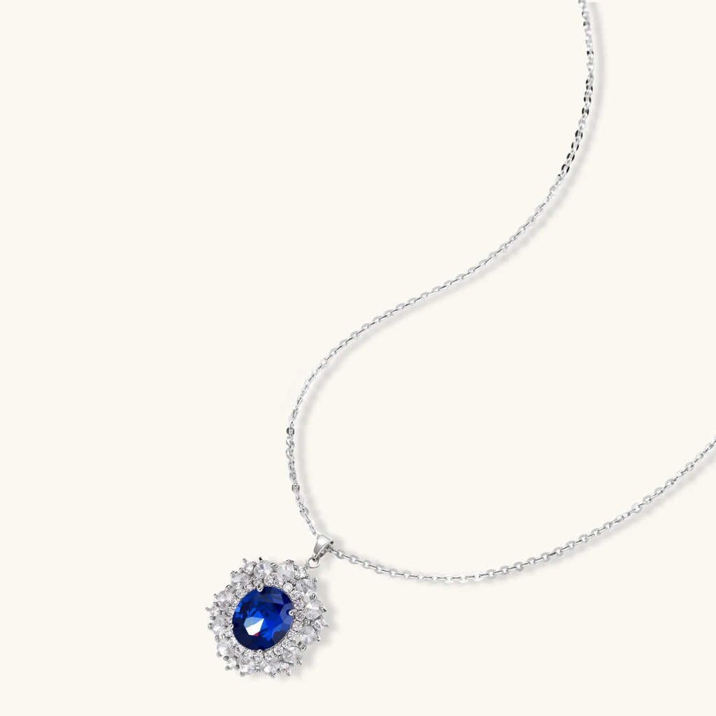 White gold plated jewelry set with blue cubic zirconia centers surrounded by clear crystal halos on cream background.