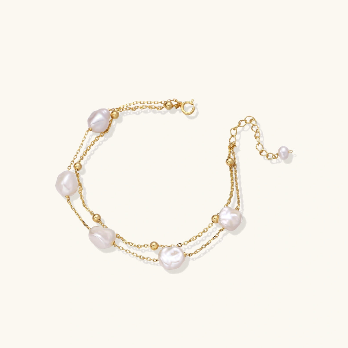 Double-strand gold bracelet with irregular baroque pearls and smooth freshwater pearls on cream background.