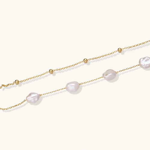 Double-strand gold bracelet with irregular baroque pearls and smooth freshwater pearls on cream background.