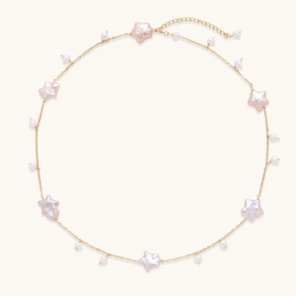 Gold vermeil chain with iridescent star-shaped baroque pearls and small round freshwater pearl drops on cream background.