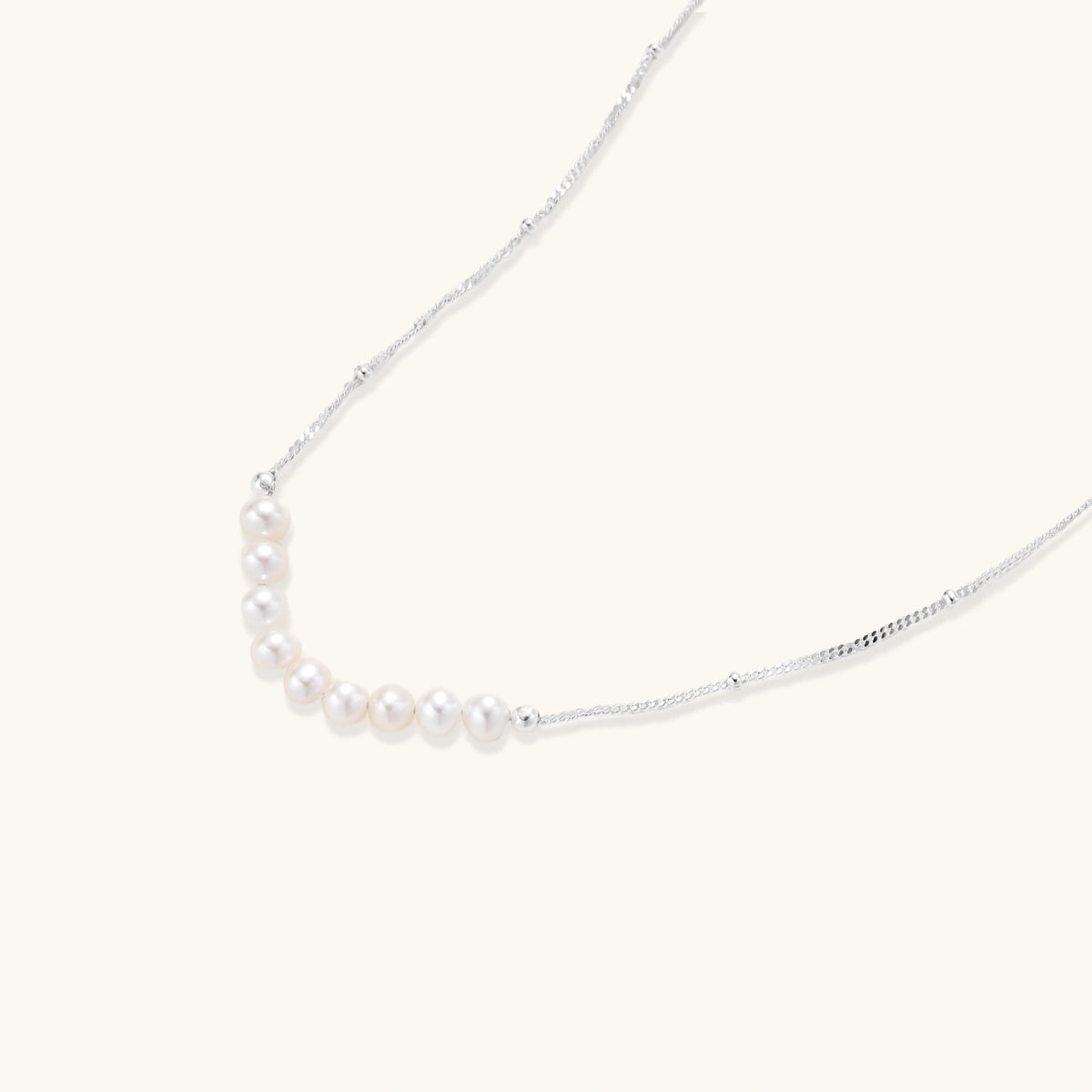Delicate sterling silver chain necklace with small freshwater pearls arranged in a curved smile arc on cream background.