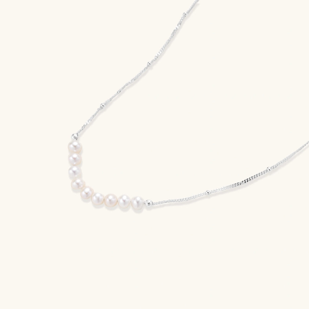 Delicate sterling silver chain necklace with small freshwater pearls arranged in a curved smile arc on cream background.