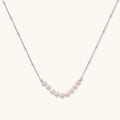 Delicate sterling silver chain necklace with small freshwater pearls arranged in a curved smile arc on cream background.