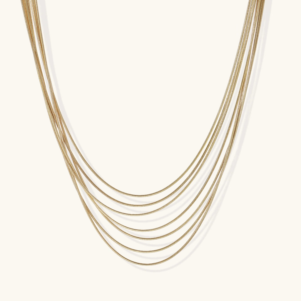 Seven delicate gold-plated snake chains create an elegant layered necklace on a neutral background.