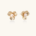 Gold-plated flower stud earrings with textured petals and centered freshwater pearl on beige background