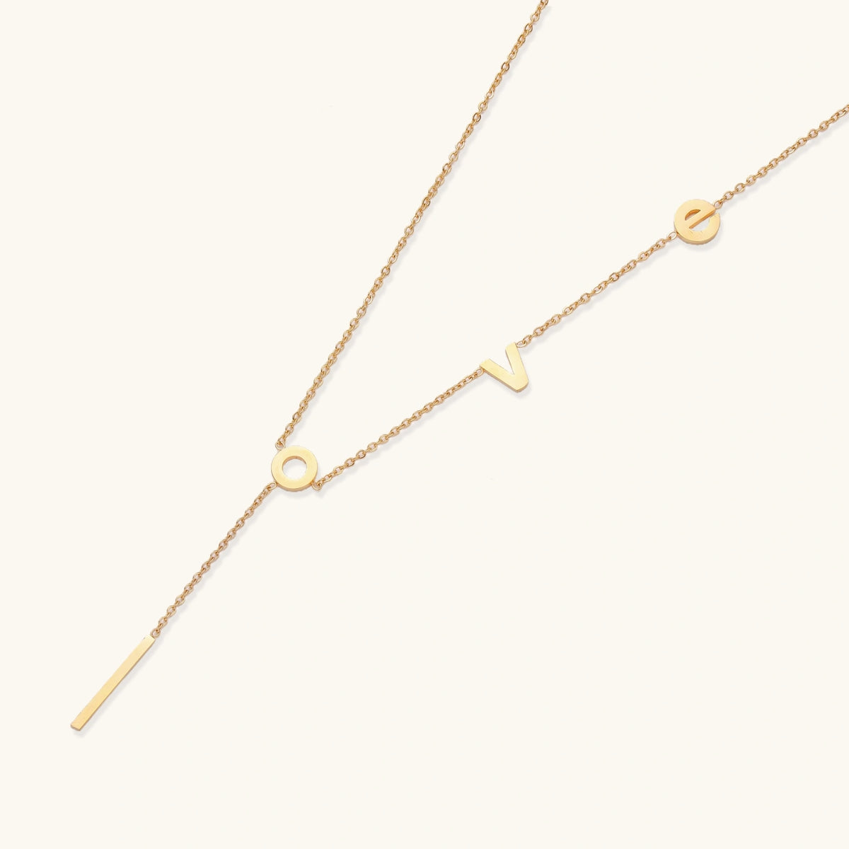 Gold Y-shaped necklace with L-O-V-E letter charms and vertical bar pendant on delicate chain against cream background