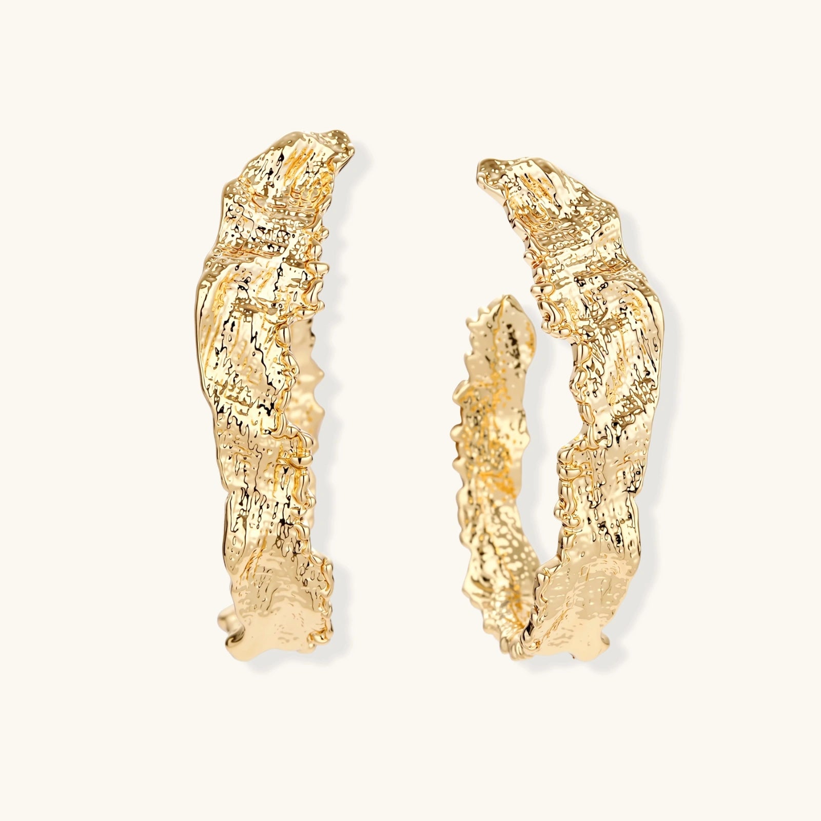 Close-up of sculptural hoop earrings with organic molten texture in silver and gold finishes on white background