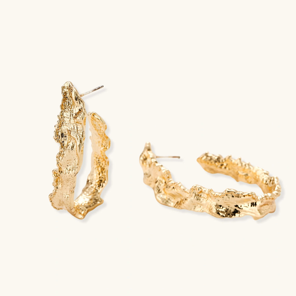 Close-up of sculptural hoop earrings with organic molten texture in silver and gold finishes on white background