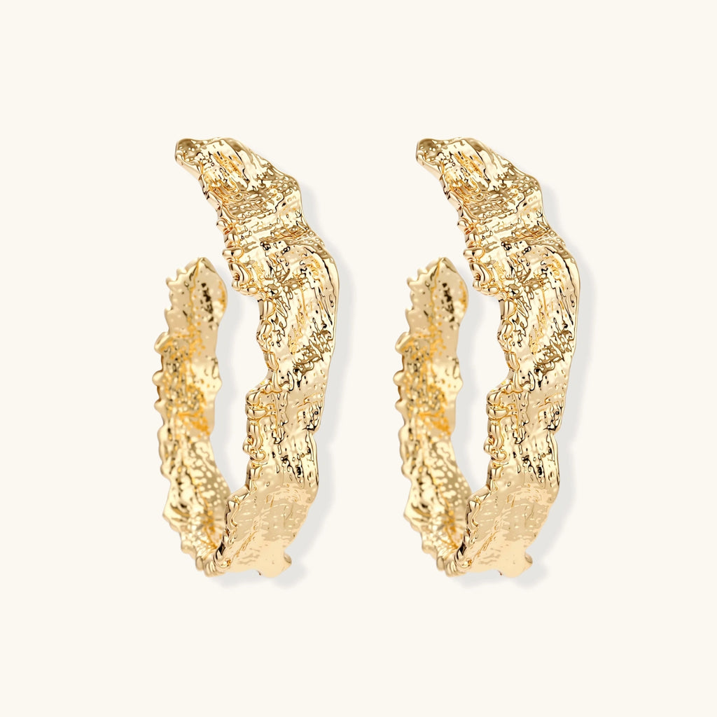 Close-up of sculptural hoop earrings with organic molten texture in silver and gold finishes on white background