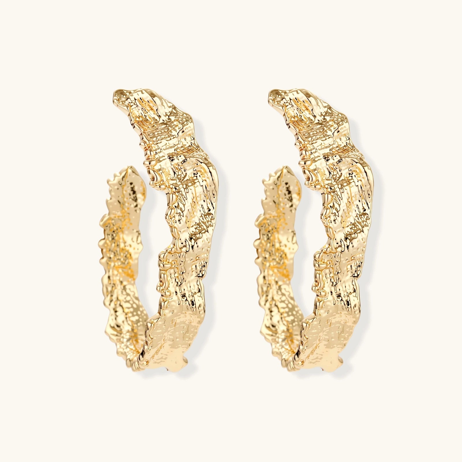 Close-up of sculptural hoop earrings with organic molten texture in silver and gold finishes on white background