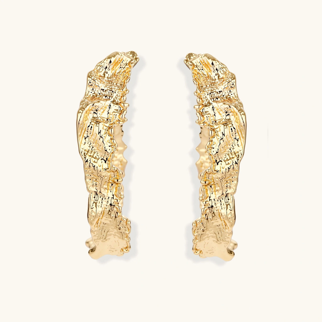 Close-up of sculptural hoop earrings with organic molten texture in silver and gold finishes on white background
