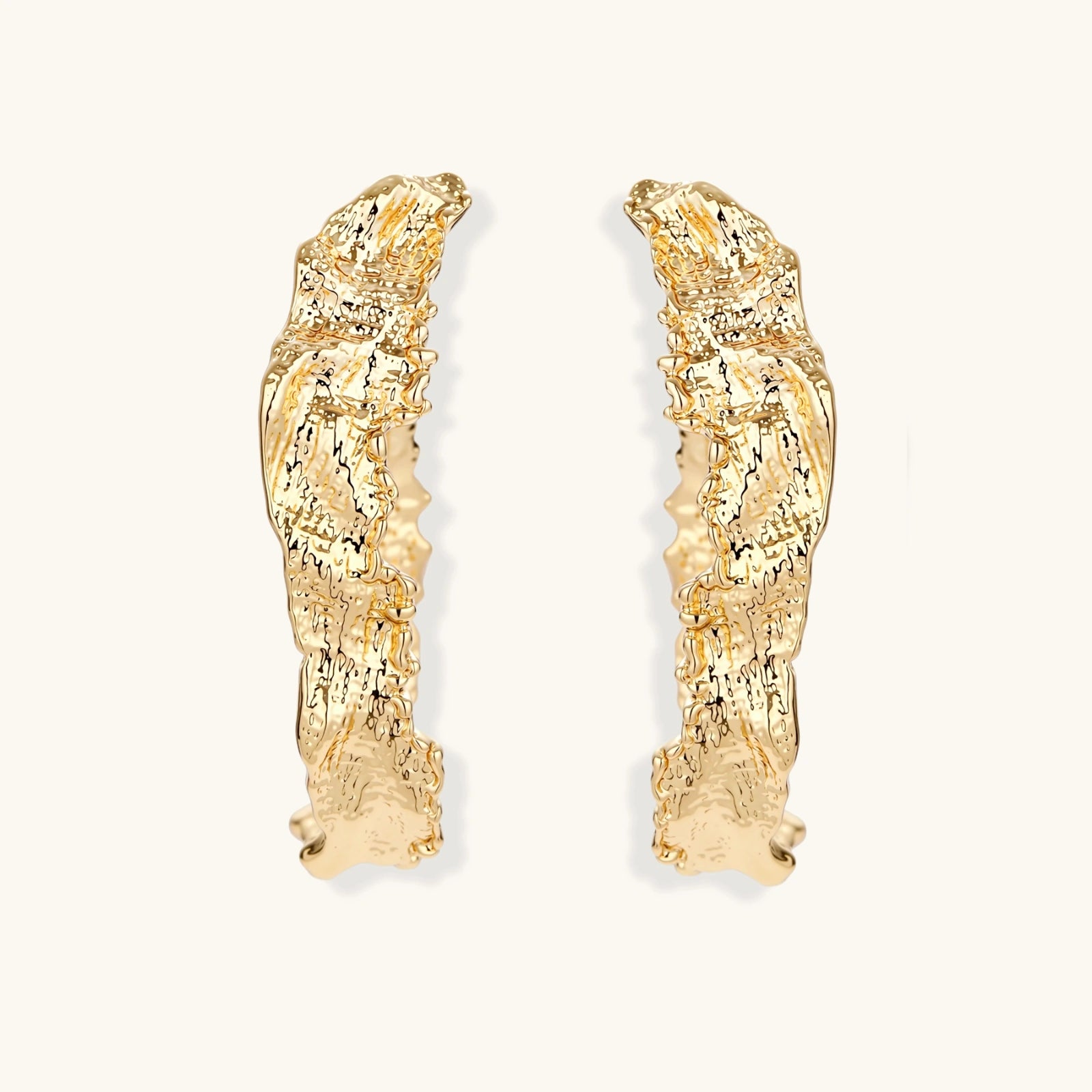 Close-up of sculptural hoop earrings with organic molten texture in silver and gold finishes on white background