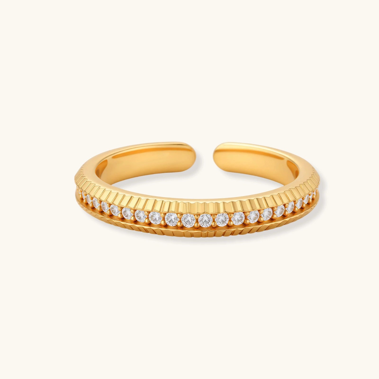 Adjustable gold-plated ring with row of sparkling crystals on ribbed band, shot against cream background