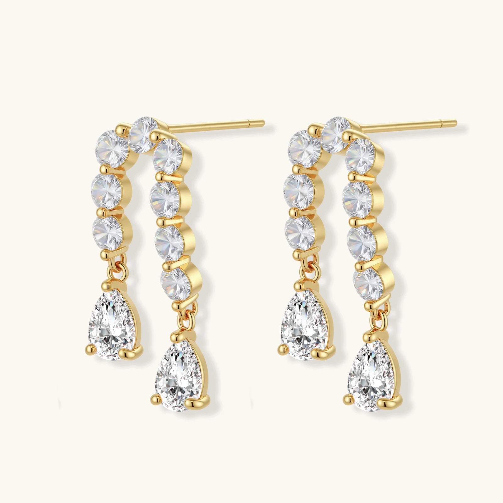 Gold-plated earrings with vertical line of clear crystals and teardrop pendants on neutral background